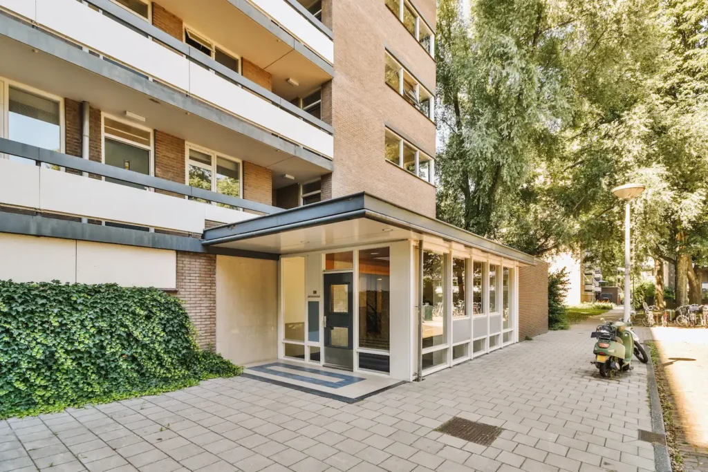 Eingang eines Mehrfamilienhauses mit Balkonen und begrüntem Vorplatz
