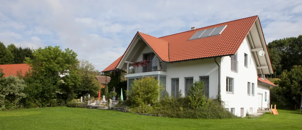 Weißes Wohnhaus mit rotem Satteldach und Garten